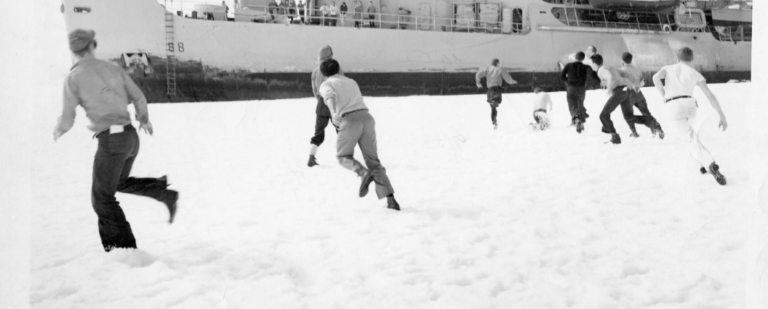People running and playing in snow, watched from a ship